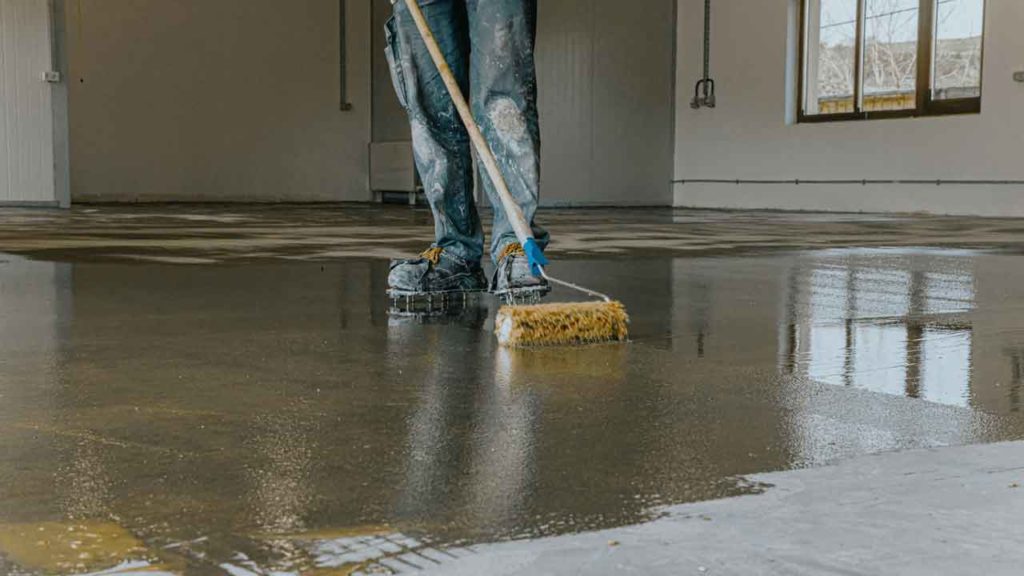 Tradesperson using a floor squeegee to spread epoxy coating across a concrete floor
