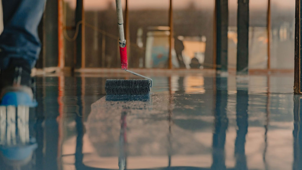 Applying a dark epoxy floor coating with a roller inside a building under construction
