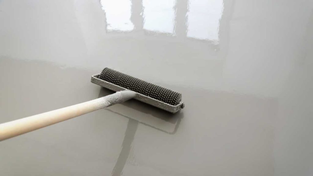 Applying a light grey epoxy topcoat to a concrete floor with a spiked roller