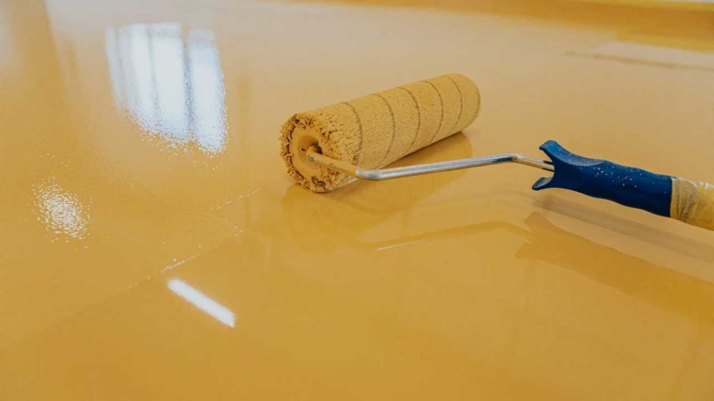 Tradesperson applying a yellow epoxy floor coating with a paint roller