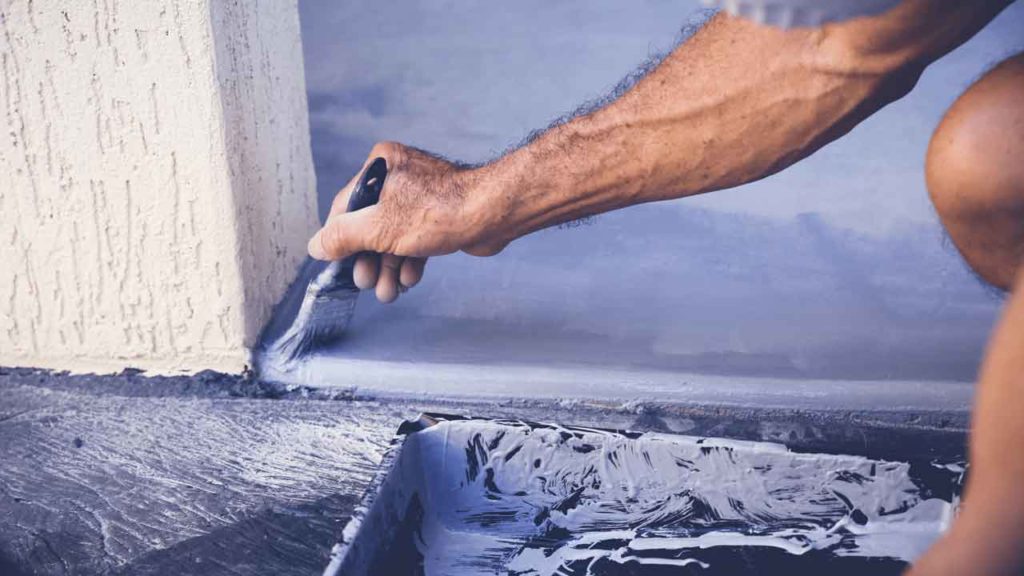 Tradesperson using a paintbrush to cut in epoxy coating along a garage wall edge