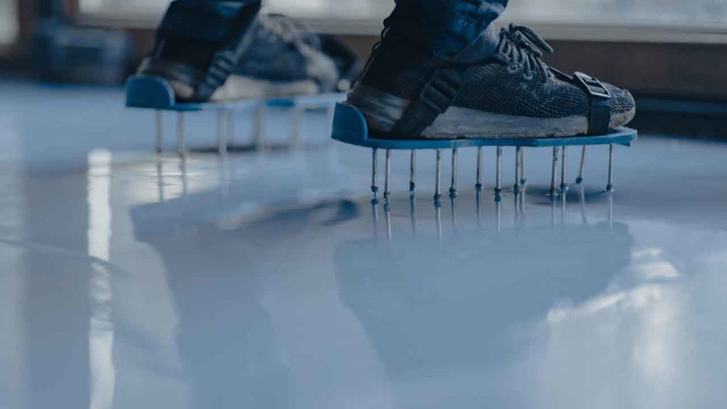 Tradesperson wearing spiked shoe attachments walking across a wet epoxy floor coating