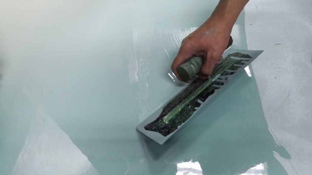 Tradesperson using a notched squeegee to spread wet epoxy resin across a garage floor